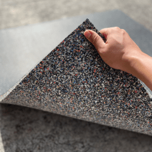 Commercial Standard Exercise mat- Flooring Mat (1000MM*1000MM*20MM) with bottom layer visible with multi-colour particles- held in place with a hand holding the edge of the mat (partly visible)