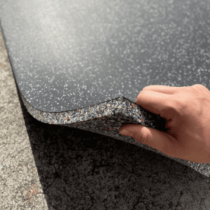 Commercial Standard Exercise mat- Flooring Mat (1000MM*1000MM*20MM) on floor with side layer visible with multi-colour particles- held in place with a hand (partly visible)