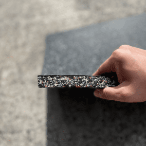 Commercial Standard Exercise mat- Flooring Mat (500MM*500MM*20MM) with side visible with multi-colour particles- held in place with a hand holding the edge of the mat (partly visible)