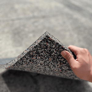 Commercial Standard Exercise mat- Flooring Mat (500MM*500MM*20MM) with bottom layer visible with multi-colour particles- held in place with a hand holding the edge of the mat (partly visible)
