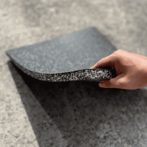 Commercial Standard Exercise mat- Flooring Mat (1000MM*1000MM*20MM) with bottom layer visible with multi-colour particles- held in place with a hand holding the edge of the mat (partly visible)